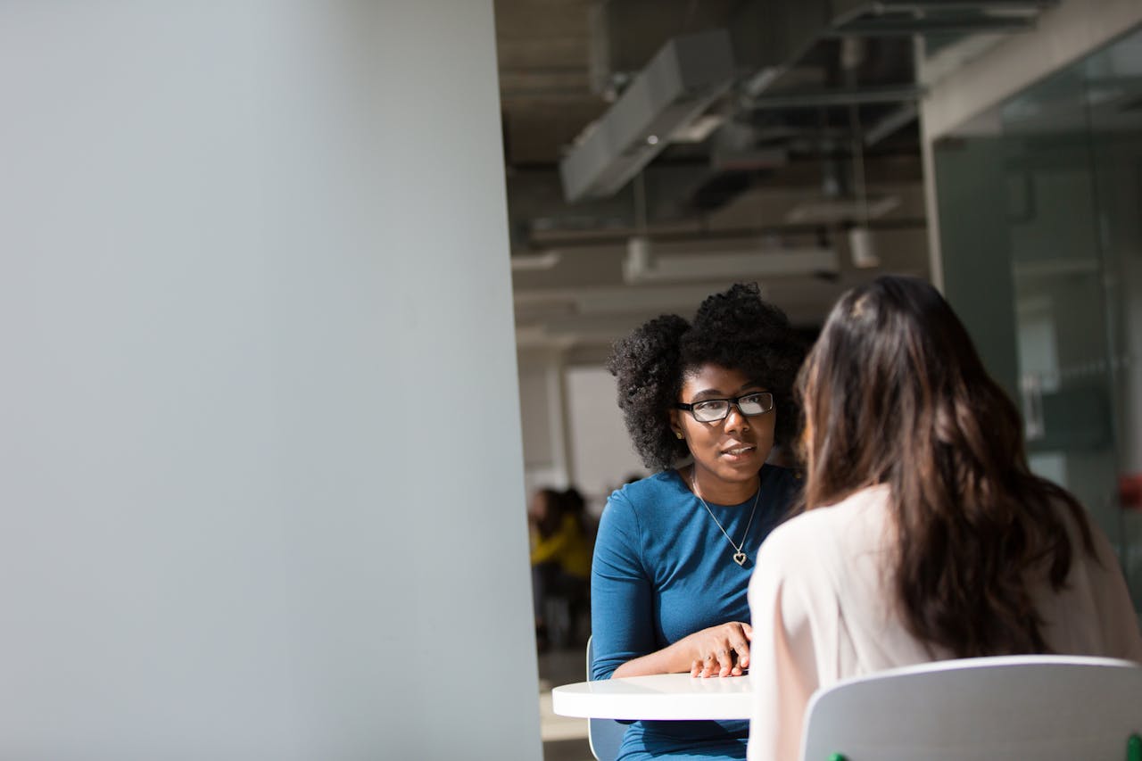 Two women engaged in a discussion in a modern office environment, highlighting communication and interaction.